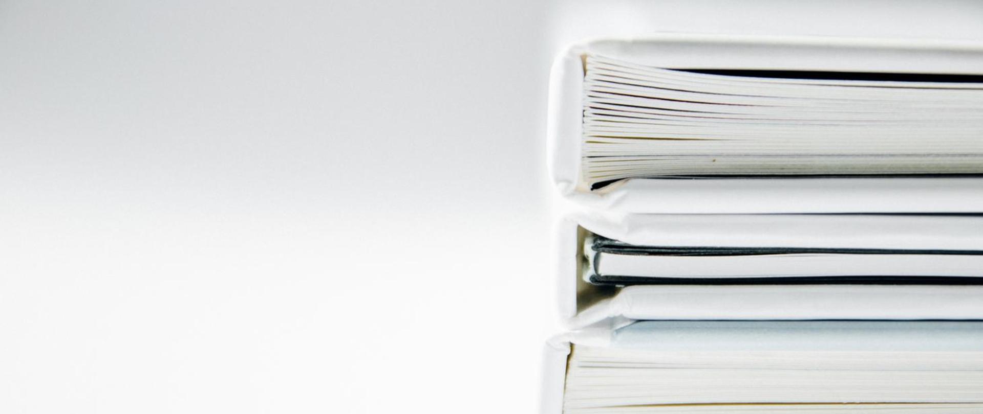 Na białym tle przedstawiony w znacznym przybliżeniu stos dokumentów.