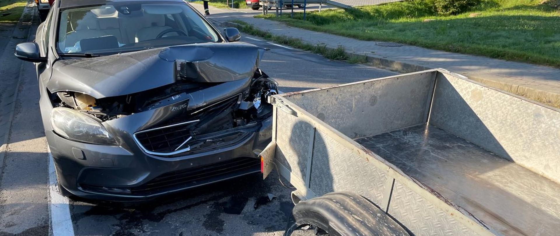 Samochód osobowy z uszkodzonym przodem oraz przyczepka samochodowa.