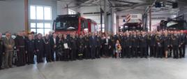 zdjęcie grupowe strażaków z uroczystej akademii w pomieszczeniu garażu na tle strażackich samochodów 
