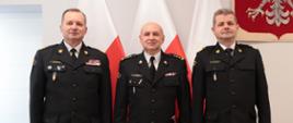 Zastępca komendanta głównego nadbryg. dr inż. Adam Konieczny, dolnośląski komendant wojewódzki nadbryg. Marek Kamiński oraz pełniący obowiązki zastępcy dolnośląskiego komendanta wojewódzkiego st.bryg. Arkadiusz Cytawa pozujący do zdjęcia na tle flag. 