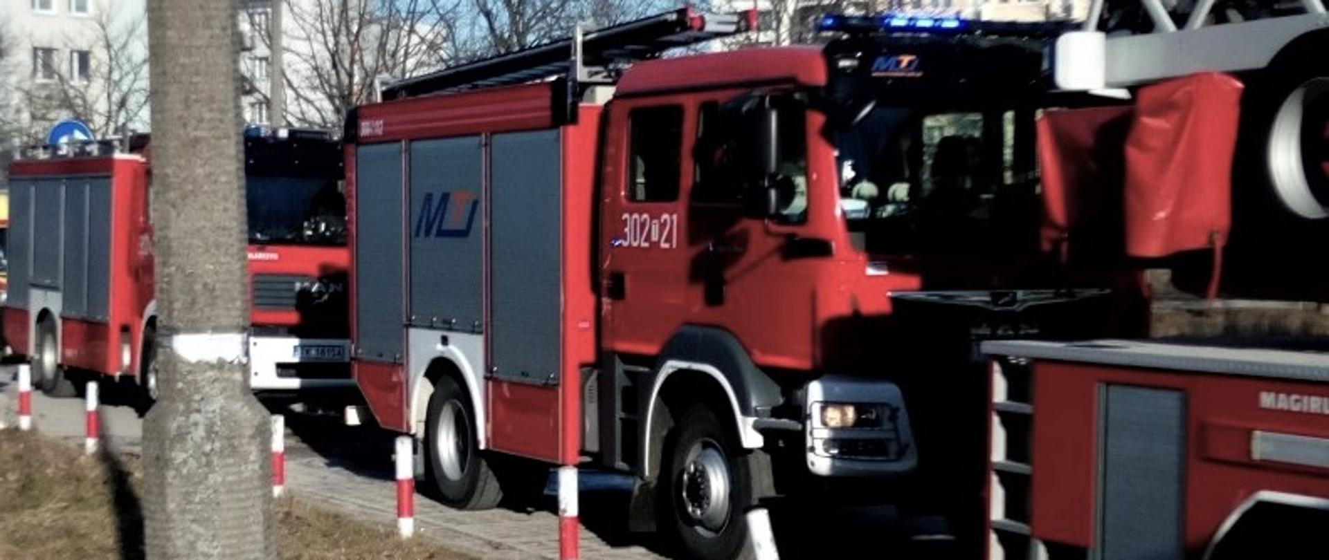 Na zdjęciu widzimy trzy samochody pożarnicze biorące udział w akcji stojące wzdłuż ciągu pieszo-jezdnego.