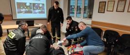 Funkcjonariusz szkoli w sali szkoleniowej druhów OSP z pierwszej pomocy przedmedycznej