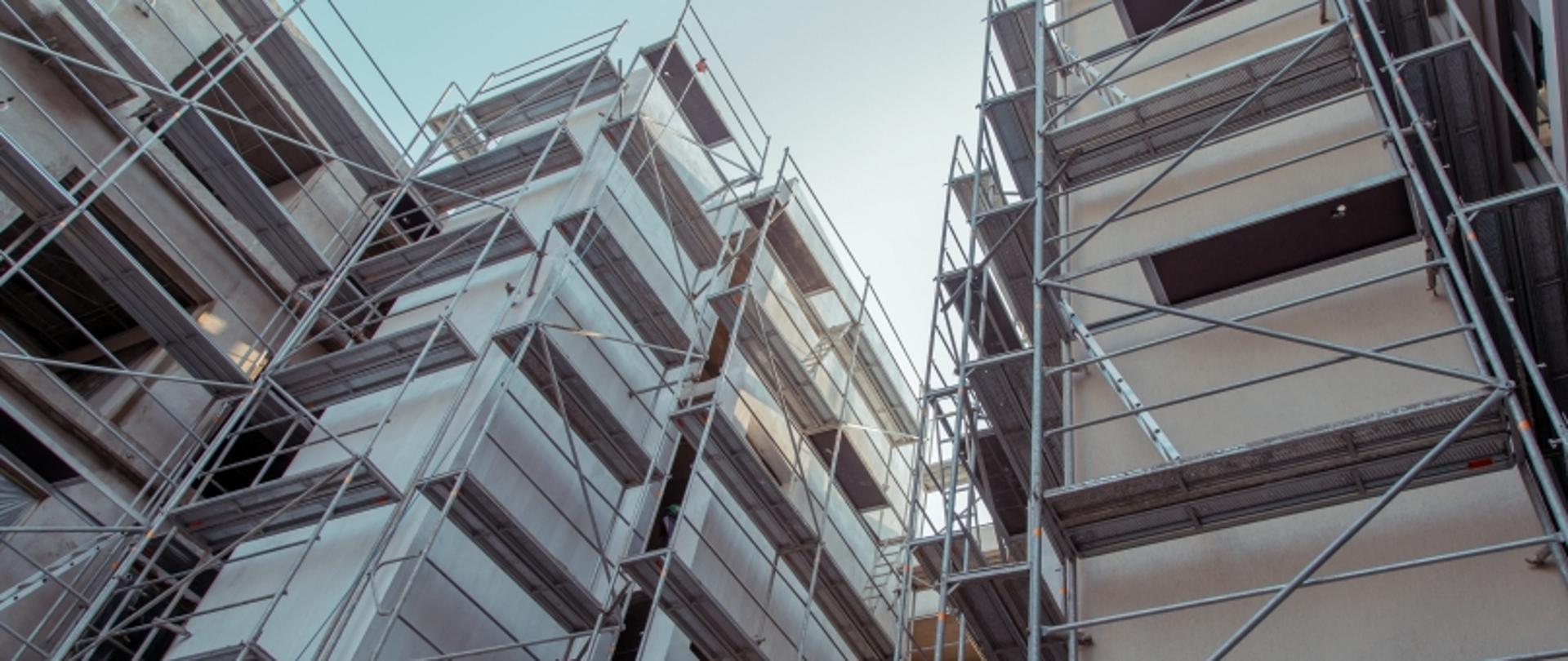 Rusztowania wokół dwóch budynków widziane z dołu.