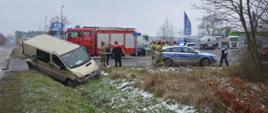 Kolizja dostawczaków. Droga gminna w Dębnie Polskim. Ogólny obraz miejsca kolizji - widok od strony Rawicza. Częściowo w rowie znajduje się renault trafic - jeden z pojazdów biorących udział w kolizji. Z prawej strony - radiowóz policyjny i wóz straży pożarnej. Obok samochodów strażacy, policjant oraz uczestnicy zdarzenia. W tle teren jednej z firm i pojazdy ciężarowe, w tym autocysterna.