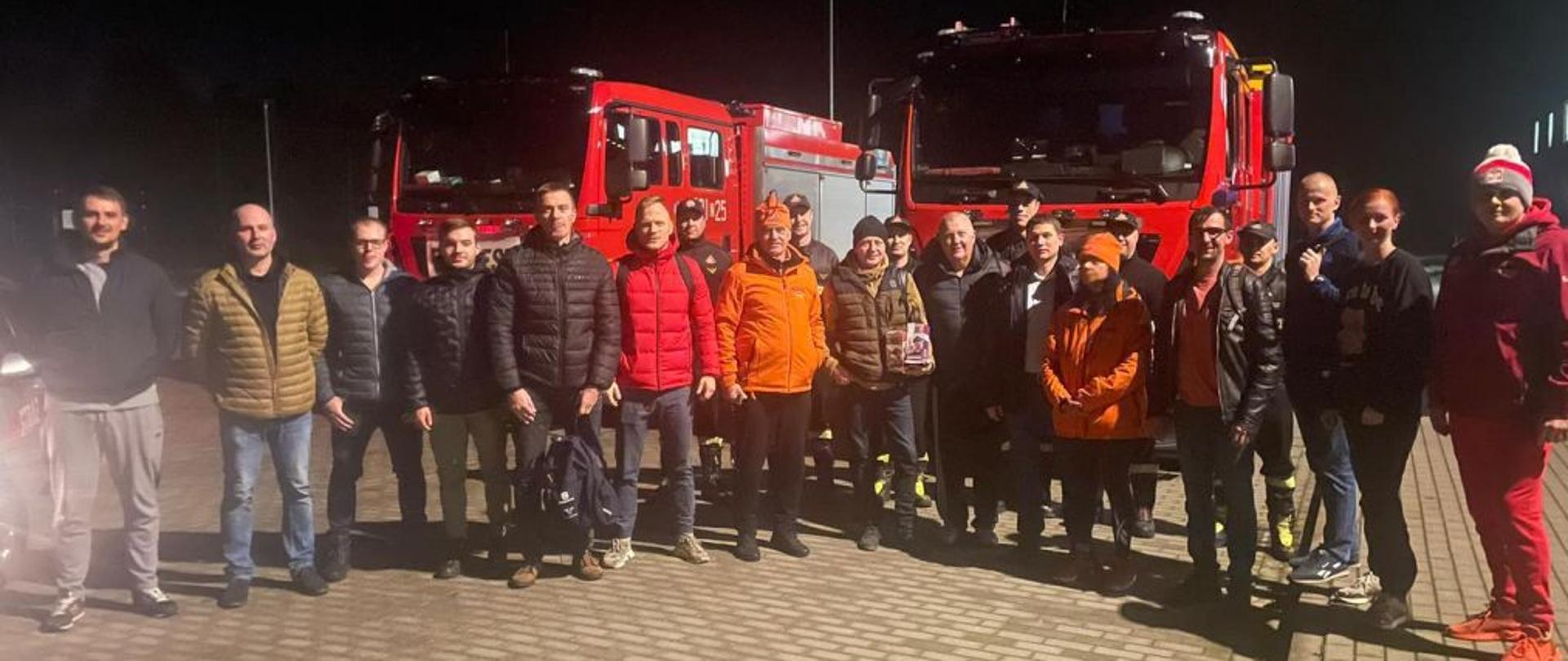 Zdjęcie grupowe strażaków uczestniczących w pływaniu. Zdjęcie wykonane w nocy. Na zdjęciu widoczni mężczyźni, ubrani w kurtki i czapki. Jest po zmierzchu, jest zimowa listopadowa noc.