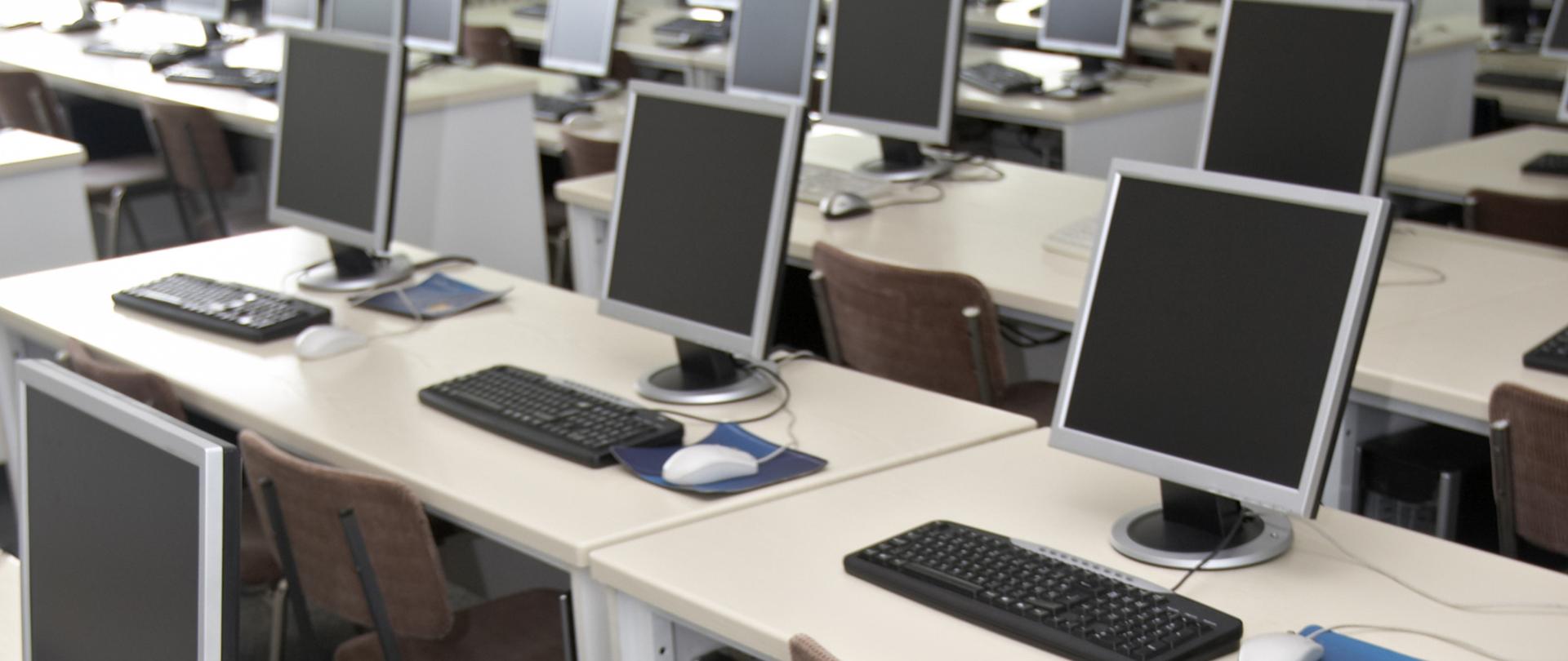 Na zdjęciu widać stanowiska komputerowe w sali lub klasie - biurka a na nich komputery.