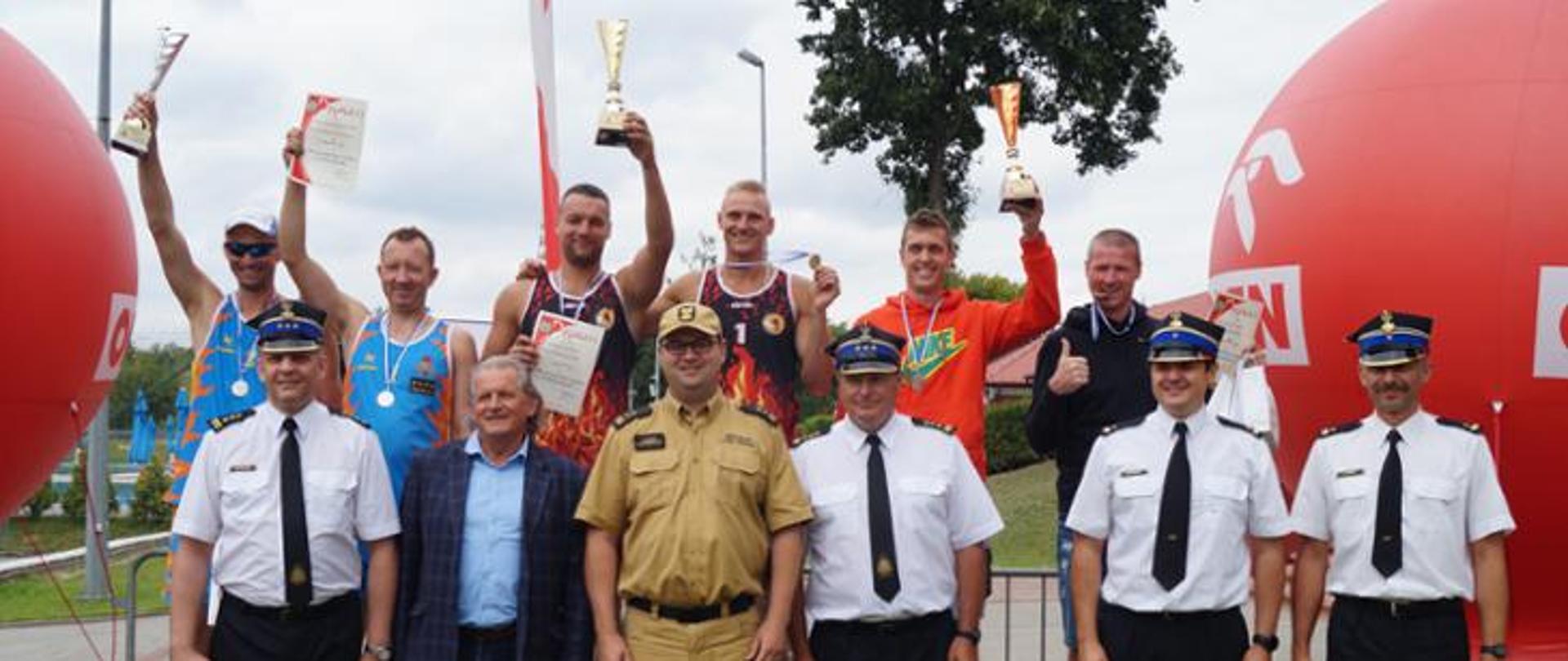 Na zdjęciu widoczni strażacy stojący na podium