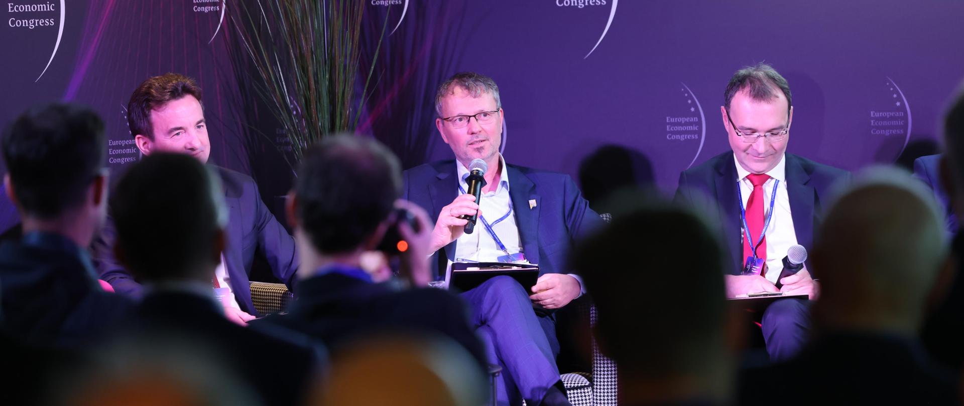 Trzech panelistów siedzi na fotelach. Po środku wiceminister Jacek Bartmiński. 