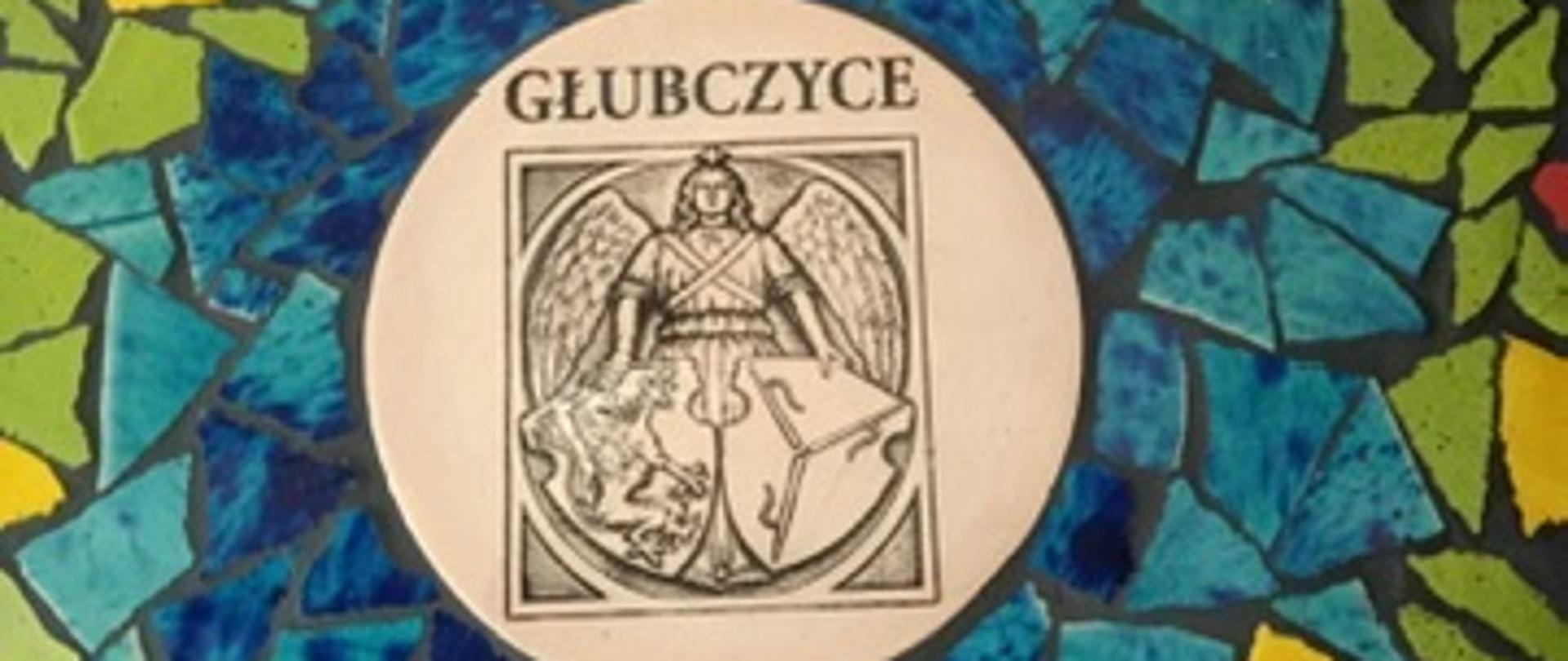 Okrągła mozaika z kawałków płytek w odcieniach niebieskiego, zielonego, żółtego i czerwonego. W środku jasny medalion z napisem „Głubczyce” i herbem miasta przedstawiającym anioła z tarczą.