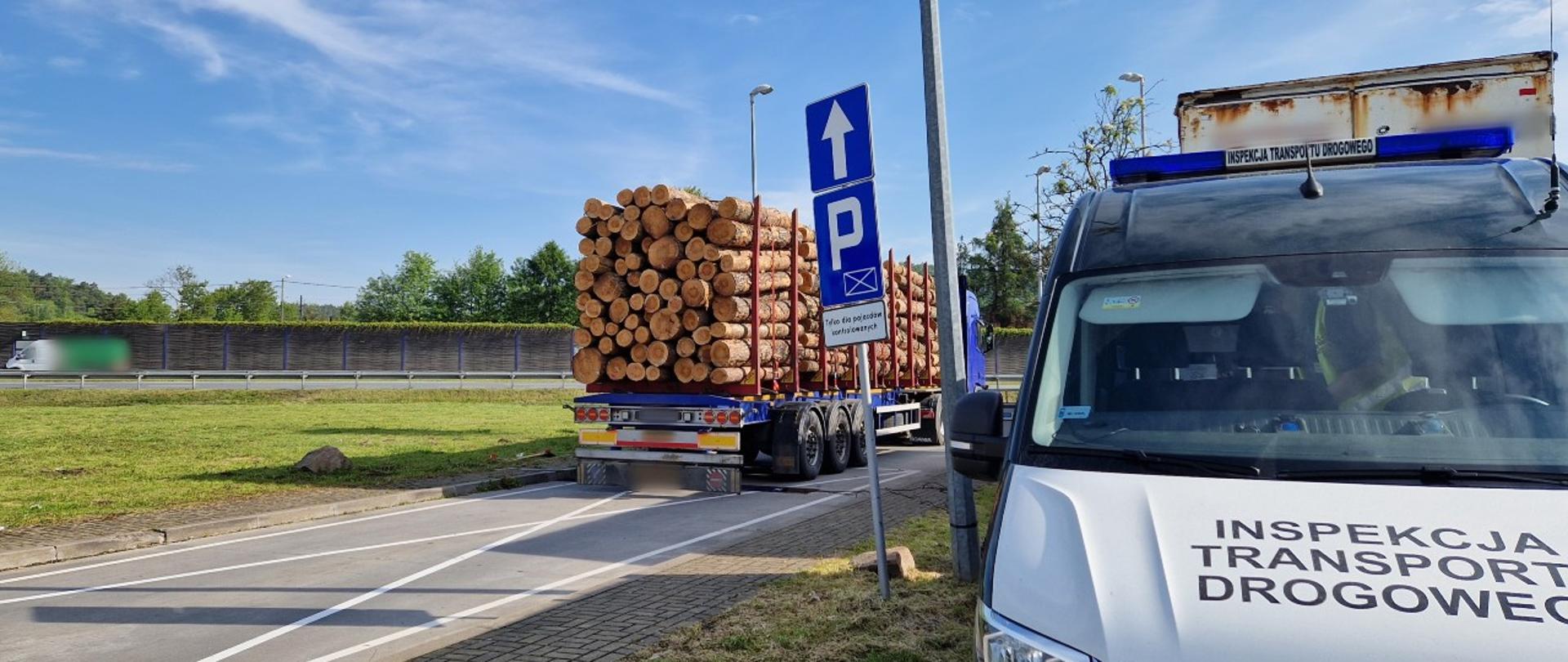 Na pierwszym planie (od prawej): przód oznakowanego furgonu małopolskiej Inspekcji Transportu Drogowego. W tle: ciągnik siodłowy z podpiętą naczepą kłonicową i przewożonym nadmiarem kłód drewna stoi tuż za wagami inspekcyjnymi.