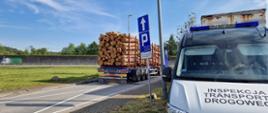 Na pierwszym planie (od prawej): przód oznakowanego furgonu małopolskiej Inspekcji Transportu Drogowego. W tle: ciągnik siodłowy z podpiętą naczepą kłonicową i przewożonym nadmiarem kłód drewna stoi tuż za wagami inspekcyjnymi.