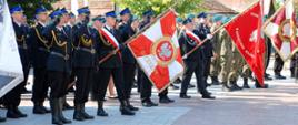 Zdjęcie zrobione na placu. Na zdjęciu widać umundurowanych mężczyzn wśród nich strażacy są to poczty sztandarowe formacji mundurowych część strażaków ma uniesioną prawą dłoń w salucie. Sztandary pocztów są pochylone. 