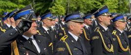 Na zdjęciu widoczni strażacy ubrani w mundury wyjściowe ze sznurem stojący podczas uroczystego apelu. Dowódca pododdziału oddaje honor pozostali strażacy stoją na baczność