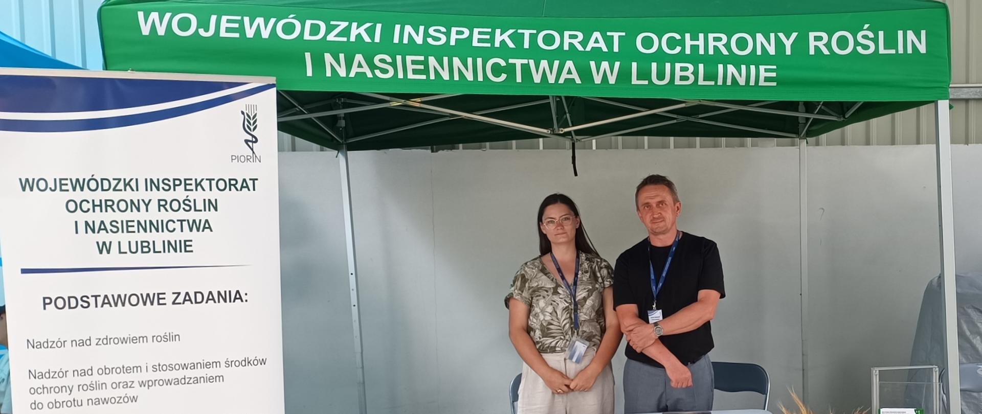 Pod namiotem stoi kobieta i mężczyzna. Na stole leżą rozłożone ulotki i materiały promocyjne. Obok stoi rolap Wojewódzkiego Inspektoratu Ochrony Roślin i Nasiennictwa z opisanymi zadaniami, które realizuje Inspekcja.