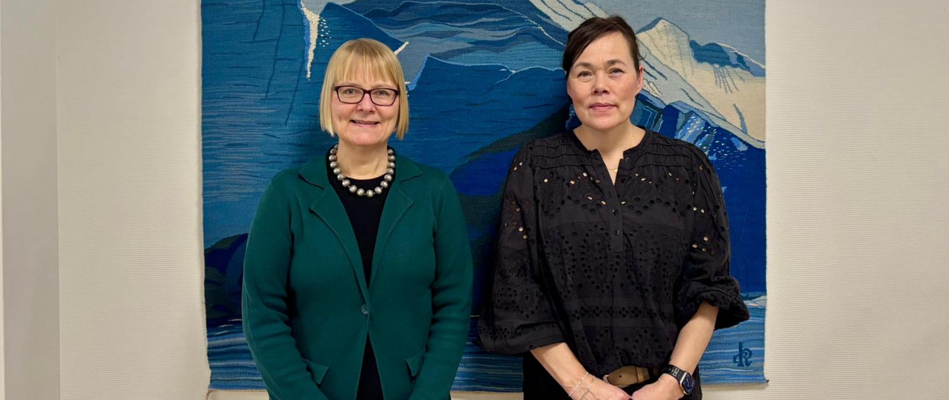 Po lewej stornie ambasador Ewa Dębska, po prawej minister spraw zagranicznych i badań naukowych Vivan Motzfeldt stojące wspólnie na tle tkaniny przedstawiającej górski pejzaż