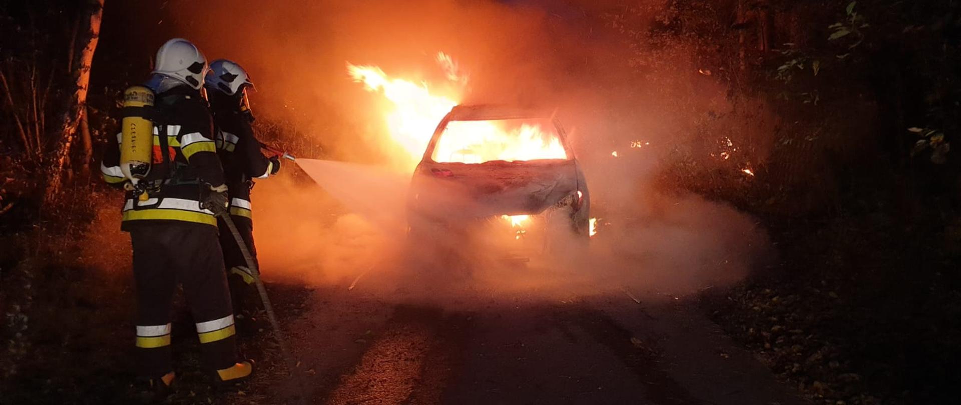 Strażacy gaszą płonący samochód osobowy.