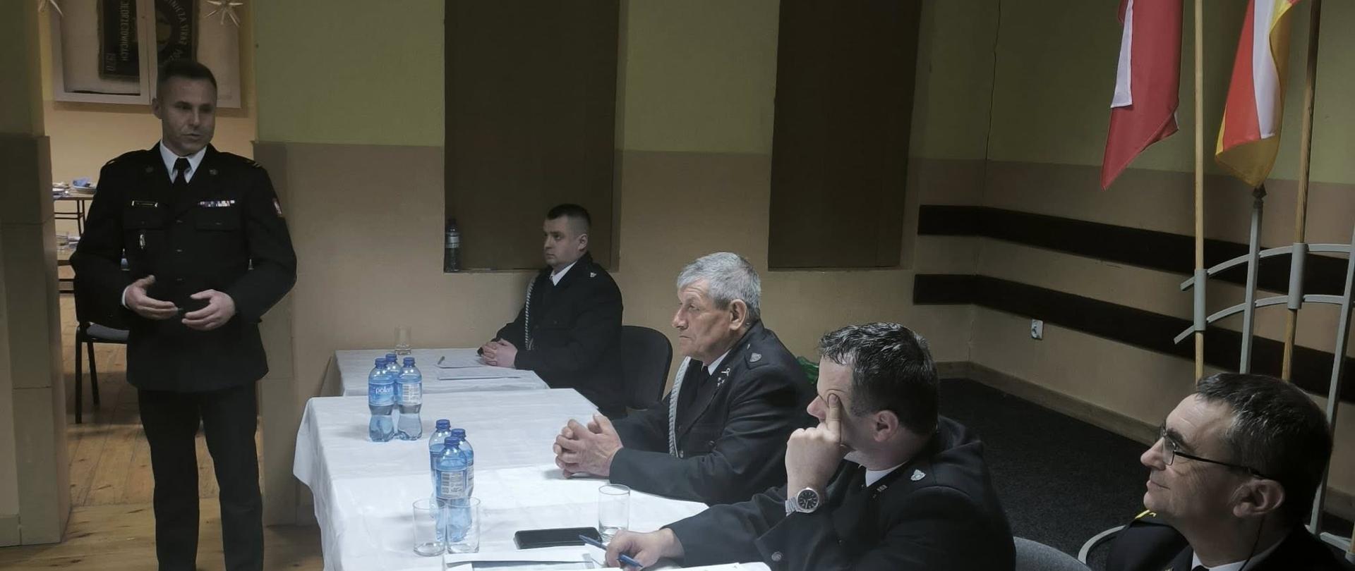 Na zdjeciu widoczny jest przemawiający Komendant Powiatowy Państowej Straży Pożarnej w Ostrowcu Świętokrzyskim młodszy brygadier Marcin Jasiński podczas zebrania sprawozdowczo-wyborczego w jednostce Ochotniczej Straży Pożarnej w Jędrzejowicach.