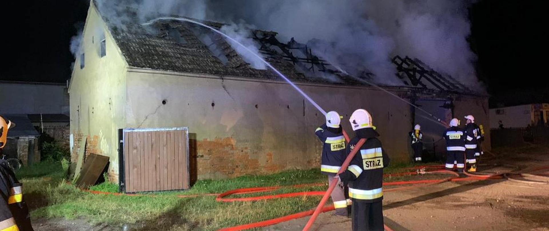 Kilu strażaków gasi pożar murowanej stodoły, jest noc, widać dym