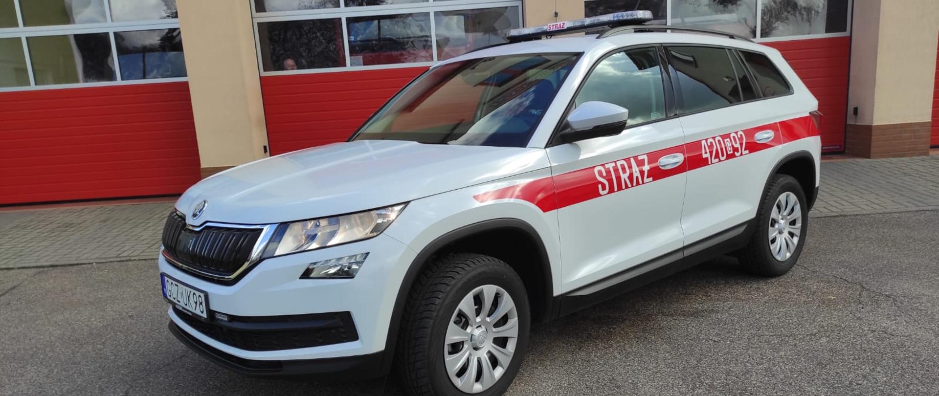 Na placu Jednostki Ratowniczo-Gaśniczej stoi samochód operacyjny Skoda Kodiaq na tle bram garażowych