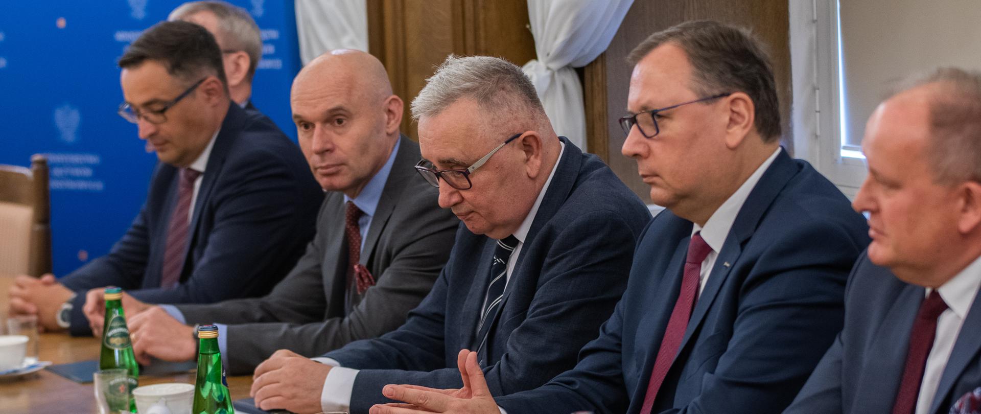 Wiceminister Piotr Pyzik siedzi za stołem wraz z innymi uczestnikami spotkania.