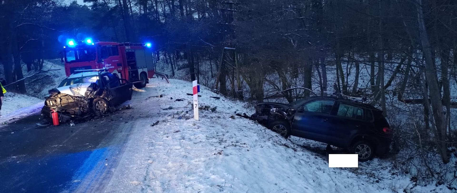 Samochód na drodze, za nim pojazd strażacki, po prawej ciemny samochód w rowie, w koło jest śnieg