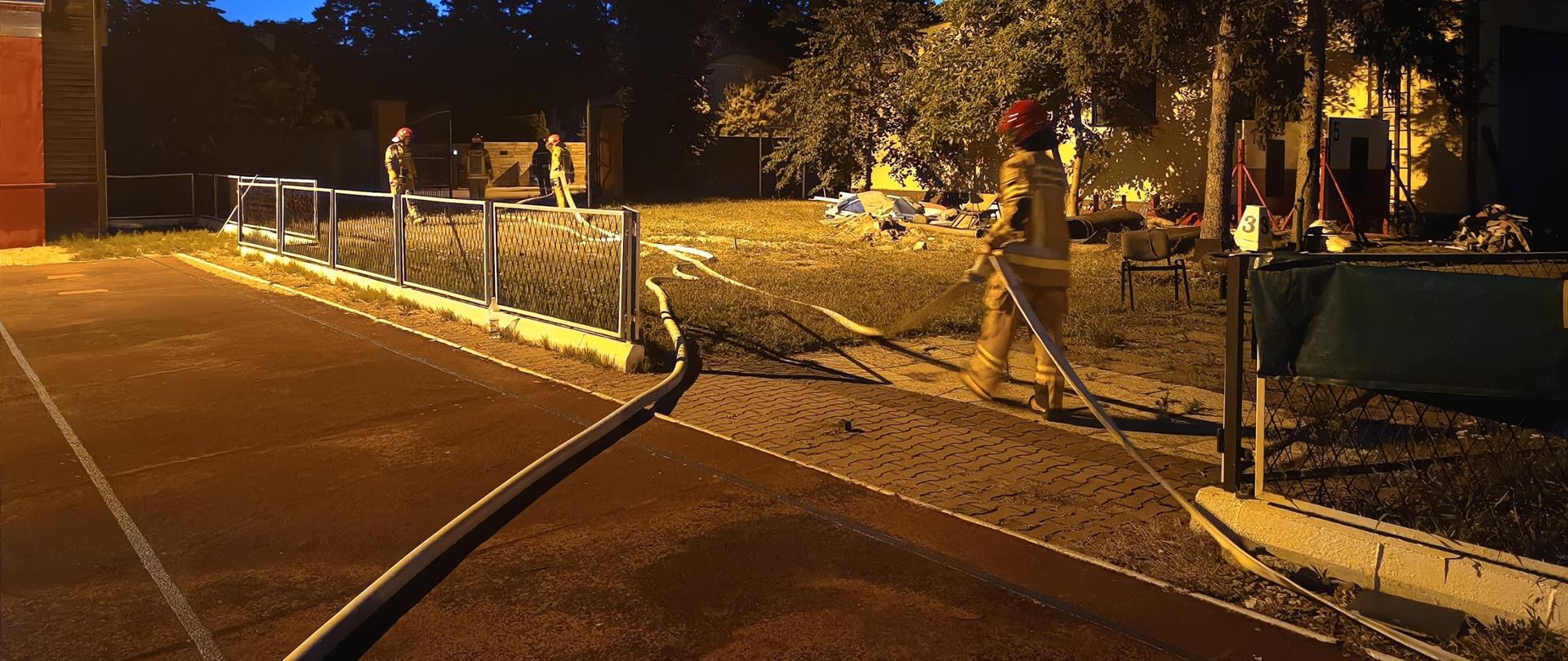 Słuchacze szkolenia podstawowego w zawodzie strażak rozciągają linie wodne podczas nocnych manewrów