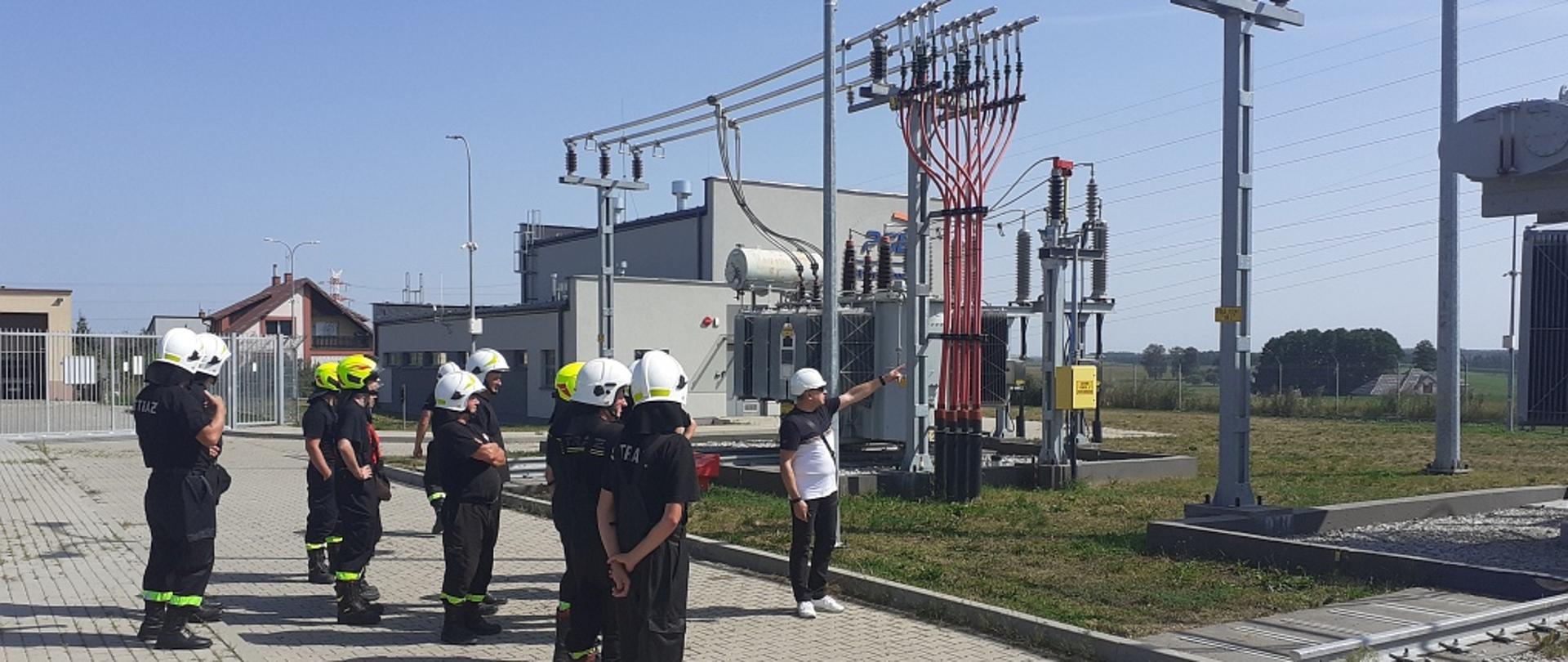 Na zdjęciu widać strażaków i pracowników PGE przed transformatorem rozdzielni.