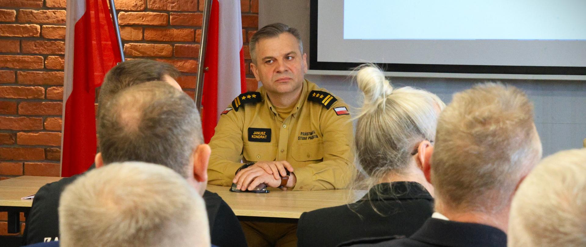 Moniecka konferencja dot. realizacji Programu Ochrony Ludności i Obrony Cywilnej - na zdjęciu st. bryg. Janusz Kondrat siedzący przy stole prezydialnym podczas konferencji, na pierwszym planie na przeciw niego zebrani goście