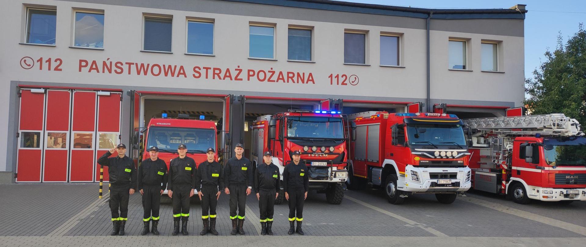 Na zdjęciu widać strażaków PSP stojących przed strażnicą, którzy oddają hołdu tragicznie zmarłemu strażakowi OSP