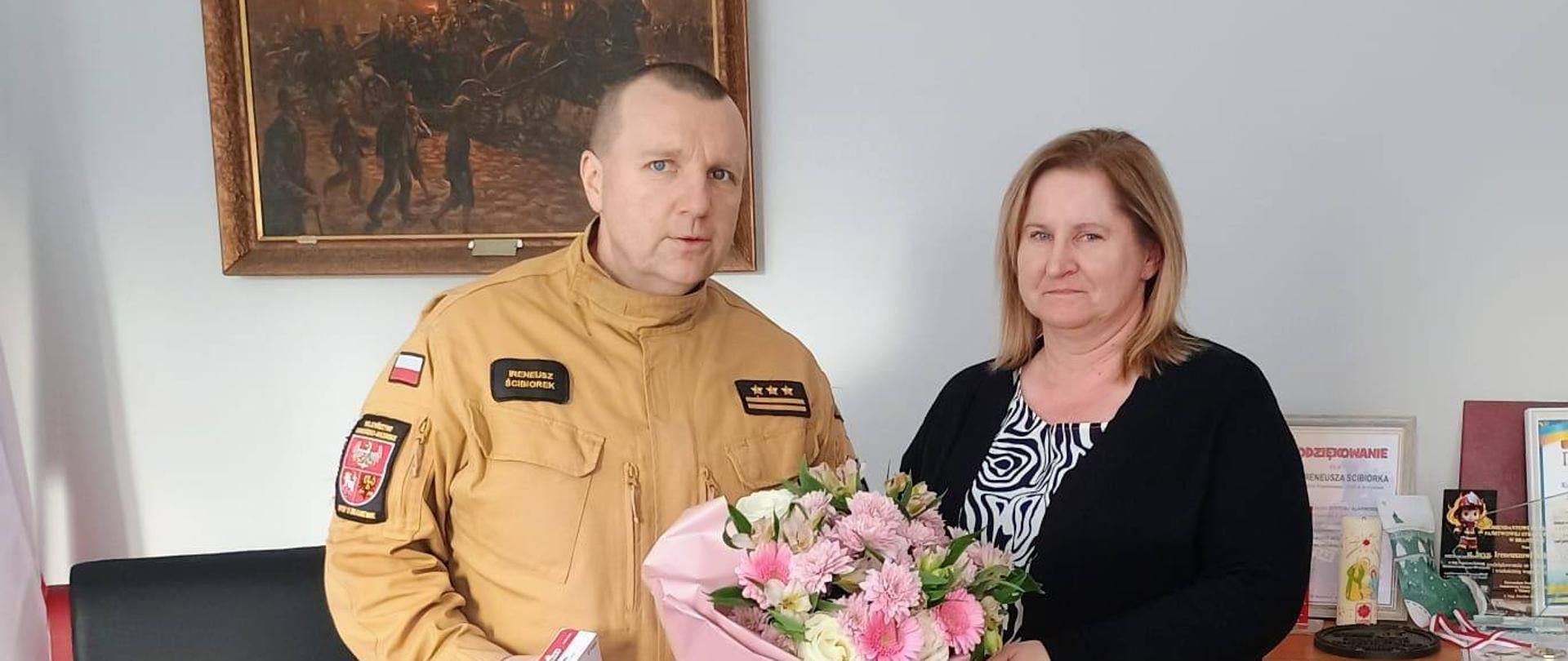 Zdjęcie zrobione w biurze. Z lewej strony stoi komendant powiatowy PSP z prawej księgowa.