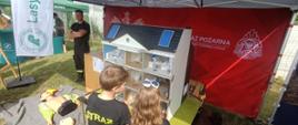Zdjęcie przedstawia dzieci oglądających symulatora zagrożeń pożarowych w domu jednorodzinnym