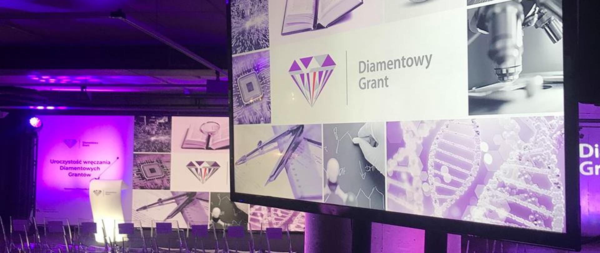 Na zdjęciu pusta, oświetlona na fioletowo sala, z boku monitor wyświetla grafiki i napis Diamentowy Grant