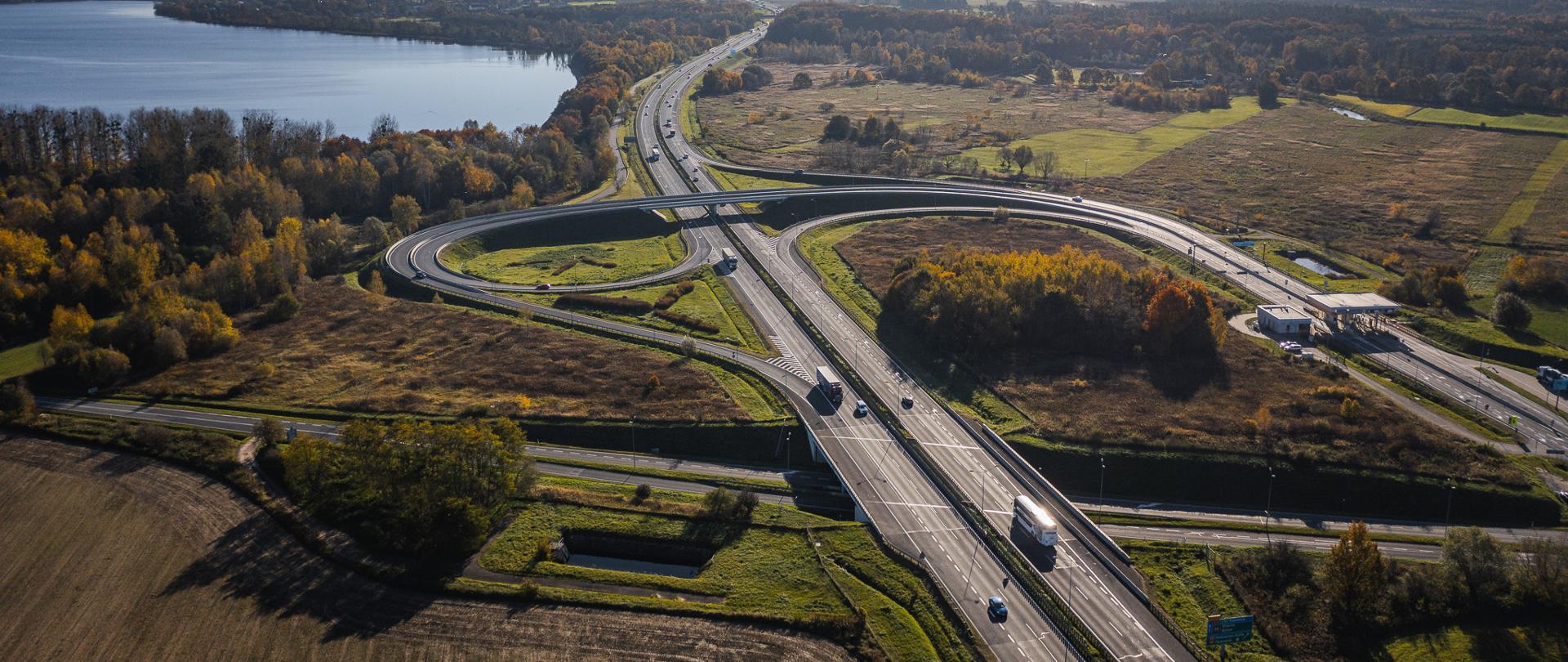 Widok z lotu ptaka na autostradę A4 i węzeł Łany, z widocznymi jezdniami, łącznicami oraz ruchem pojazdów, w otoczeniu terenów zielonych i pól.