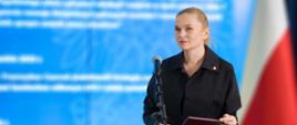 Minister Nowacka stoi i przy mikrofonie w tle duży ekran z prezentacją