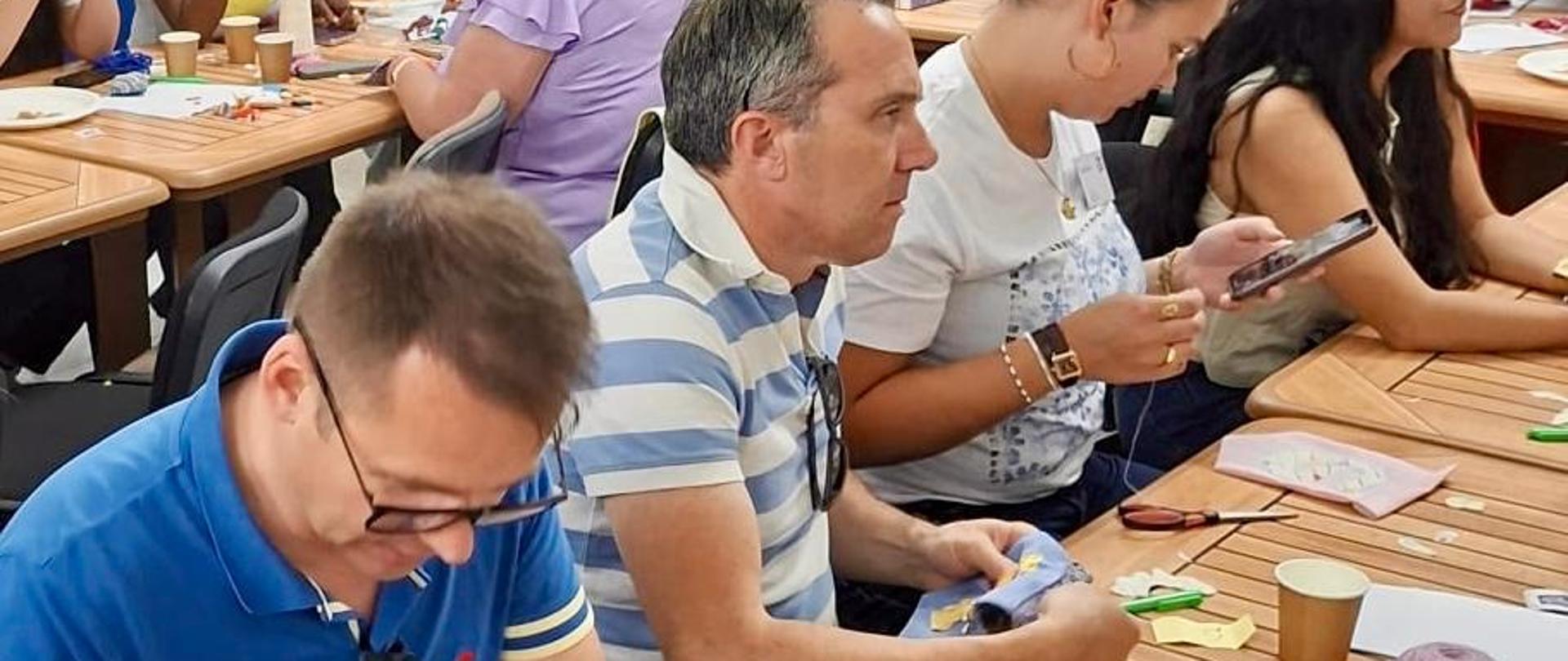 Grupa ludzi siedzących przy stołach i wspólnie szyjących w ramach wydarzenia The_Courage_to_Learn.