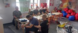Zdjęcie przedstawia funkcjonariuszy Straży Granicznej obserwujących szkolenie prowadzone przez strażaka Komendy Powiatowej Państwowej Straży Pożarnej w Gołdapi na jednym z uczestników w zakresie techniki pierwszej pomocy w przypadku zadławienia realizowane w sali edukacyjnej strażnicy