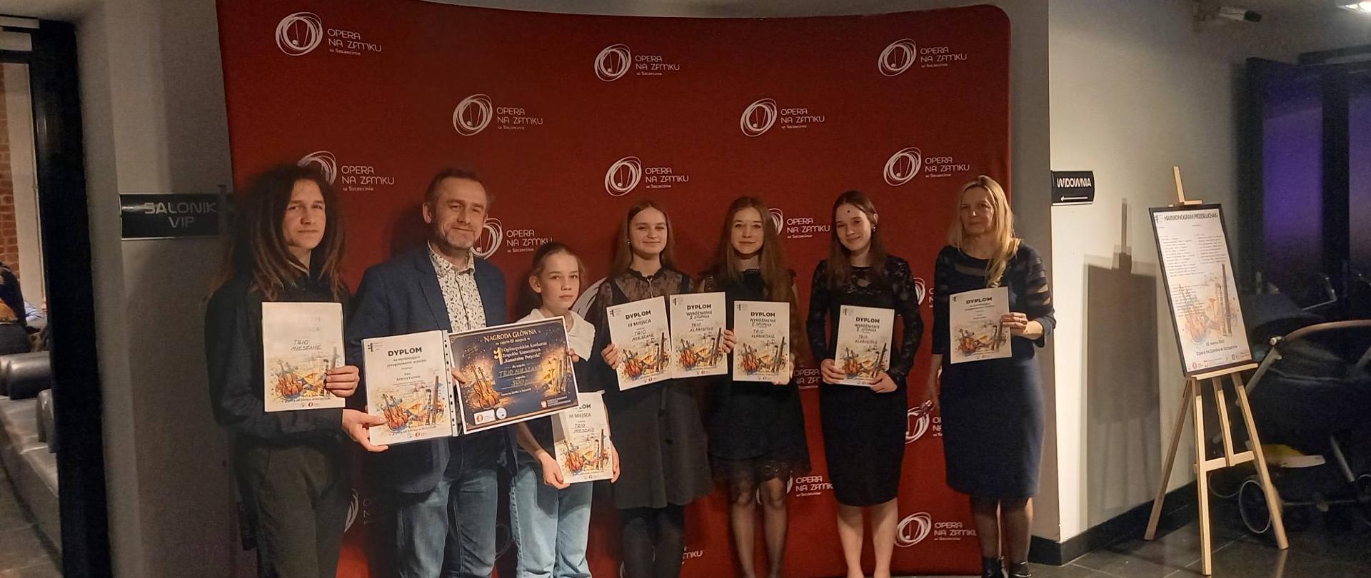Andrzej Formela i Anna Łysko pozują na stojąco wraz z uczestnikami konkursu. Wszyscy trzymają dyplomy.