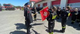 Zdjęcie przedstawia teren Jednostki Ratowniczo-Gaśniczej oraz strażaków ubranych w mundury galowe koloru czarnego ze sznurem galowym oraz czapką rogatywką na głowie, podczas obchodów Dnia Strażaka w Radziejowie. Na zdjęciu uczniowie klas mundurowych Zespołu Szkół Rolnicze Centrum Kształcenia Ustawicznego w Przemystce podczas składania roty ślubowania na Sztandar Oddziału Powiatowego Związku Ochotniczych Straży Pożarnych