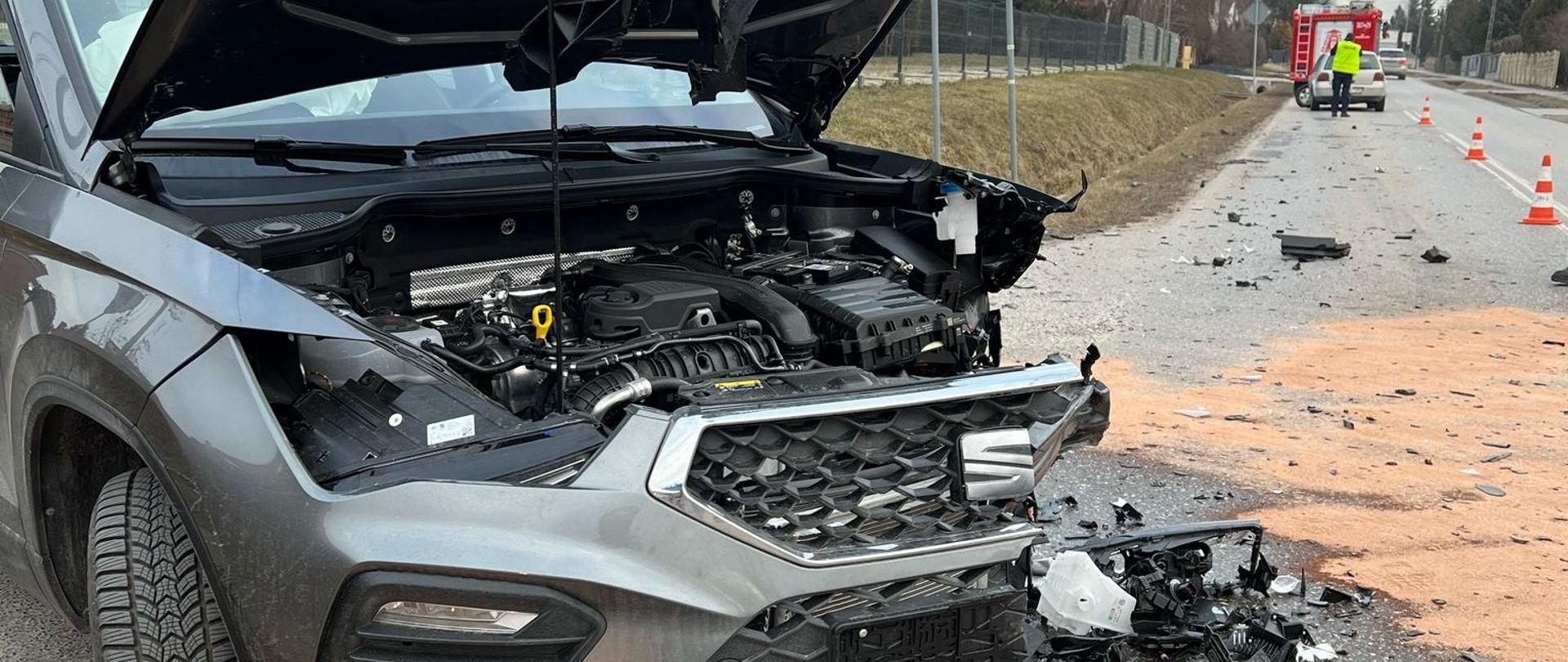 Zdjęcie przedstawia jeden ze zniszczony w wyniku zderzenia samochodów. W głębi , po prawej stronie widać drugi z pojazdów i samochód pożarniczy.