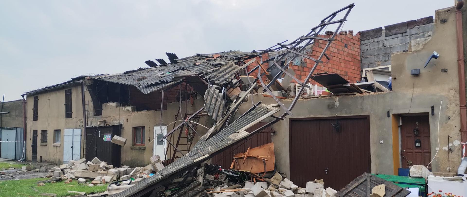 Znacznie zniszczony budynek gospodarczy po przejściu nawałnicy. Zawalony dach i fragmenty ścian oraz gruz i konstrukcja dachowa zalegają na podwórzu.