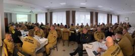 Sala szkoleniowa, trwa narada, strażacy siedzą przy stołach.