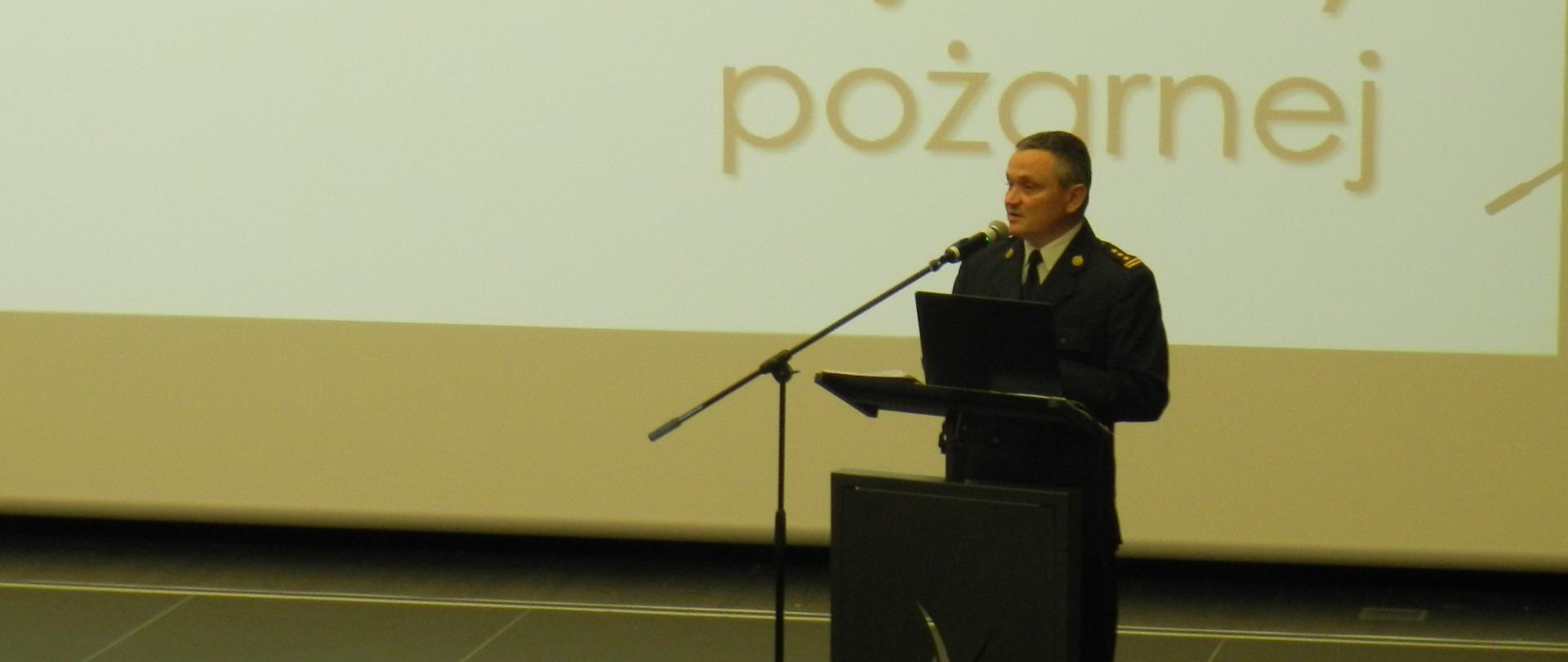 Na zdjęciu za mównicą stoi strażak w mundurze wyjściowym, przemawia, z tył napis "Projekt ustawy ochotniczej straży pożarnej".