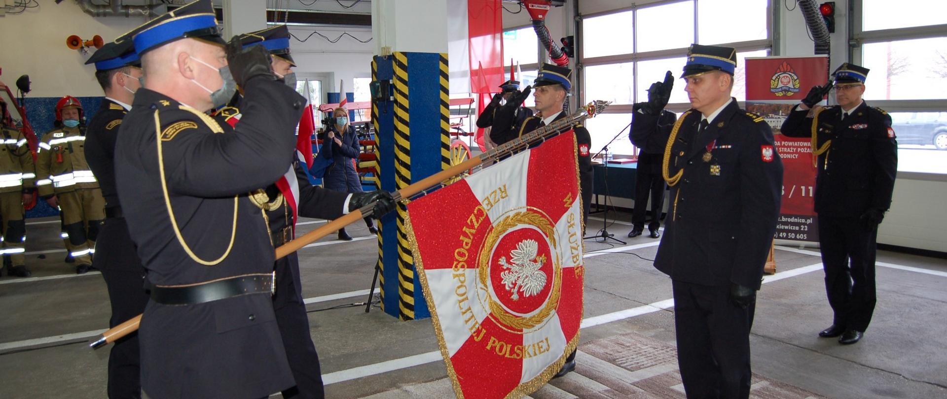 Zdjęcie przedstawia moment przekazania sztandaru KP PSP w Brodnicy. W tle pracownicy Komendy.