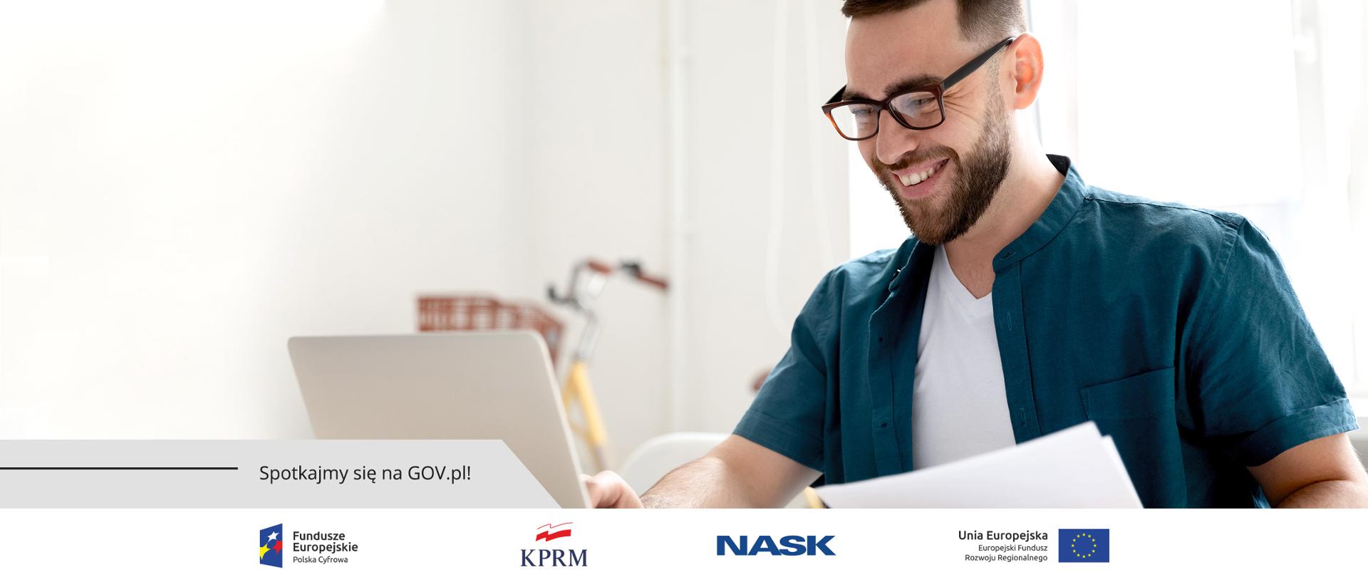 Uśmiechnięty, siedzący przed laptopem mężczyzna.