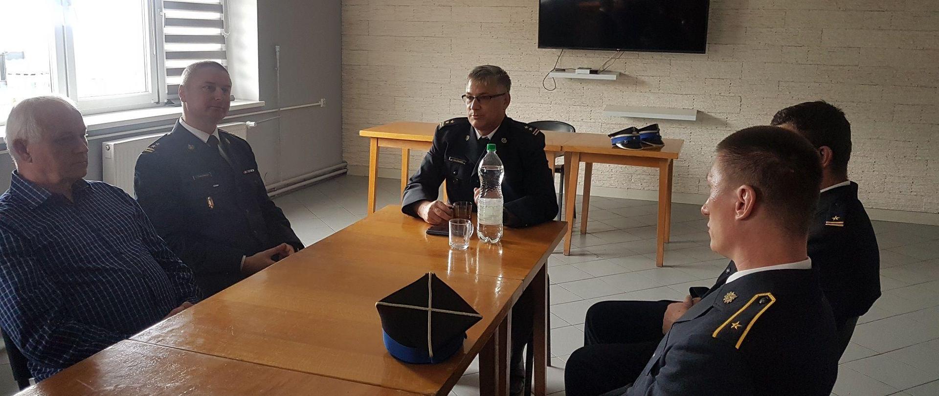 Zdjęcie ze spotkania Komendanta Wojewódzkiego PSP w Toruniu z załogą KP PSP w Aleksandrowie Kujawskim. Zdjęcie przedstawia siedzących strażaków i pracowników cywilnych przy stole na świetlicy JRG w Aleksandrowie Kujawskim