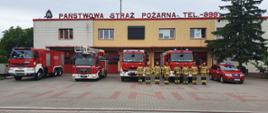 Strażacy oraz samochody ratowniczo-gaśnicze stoją przed garażami z włączonymi sygnałami świetlno-dźwiękowymi.