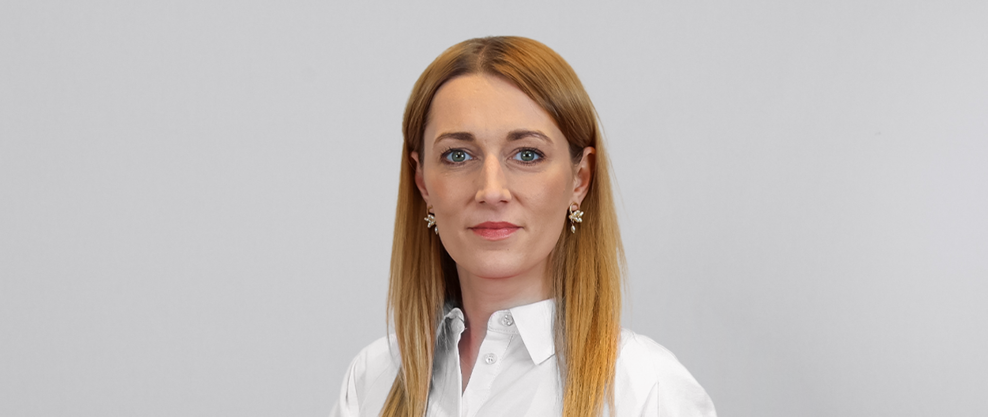 Rzeczniczka Żyto w białej bluzce stoi na tle jasnoszarej ściany.