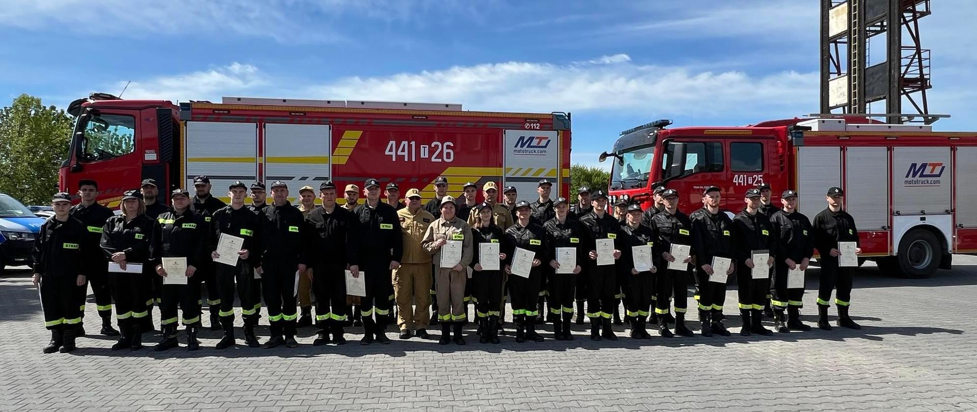 Uczestnicy kursu OSP na tle samochodów pożarniczych
