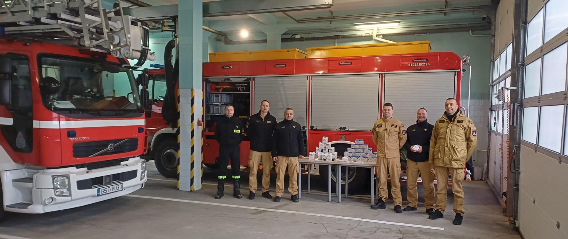 Na zdjęciu w sąsiedztwie samochodu pożarniczego stoją przedstawiciele KP PSP Starogard Gdański podczas akcji wręczania czujek czadu