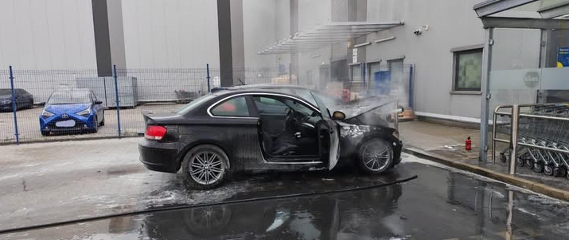 Samochód osobowy, który zapalił się na parkingu przy sklepie spożywczym 